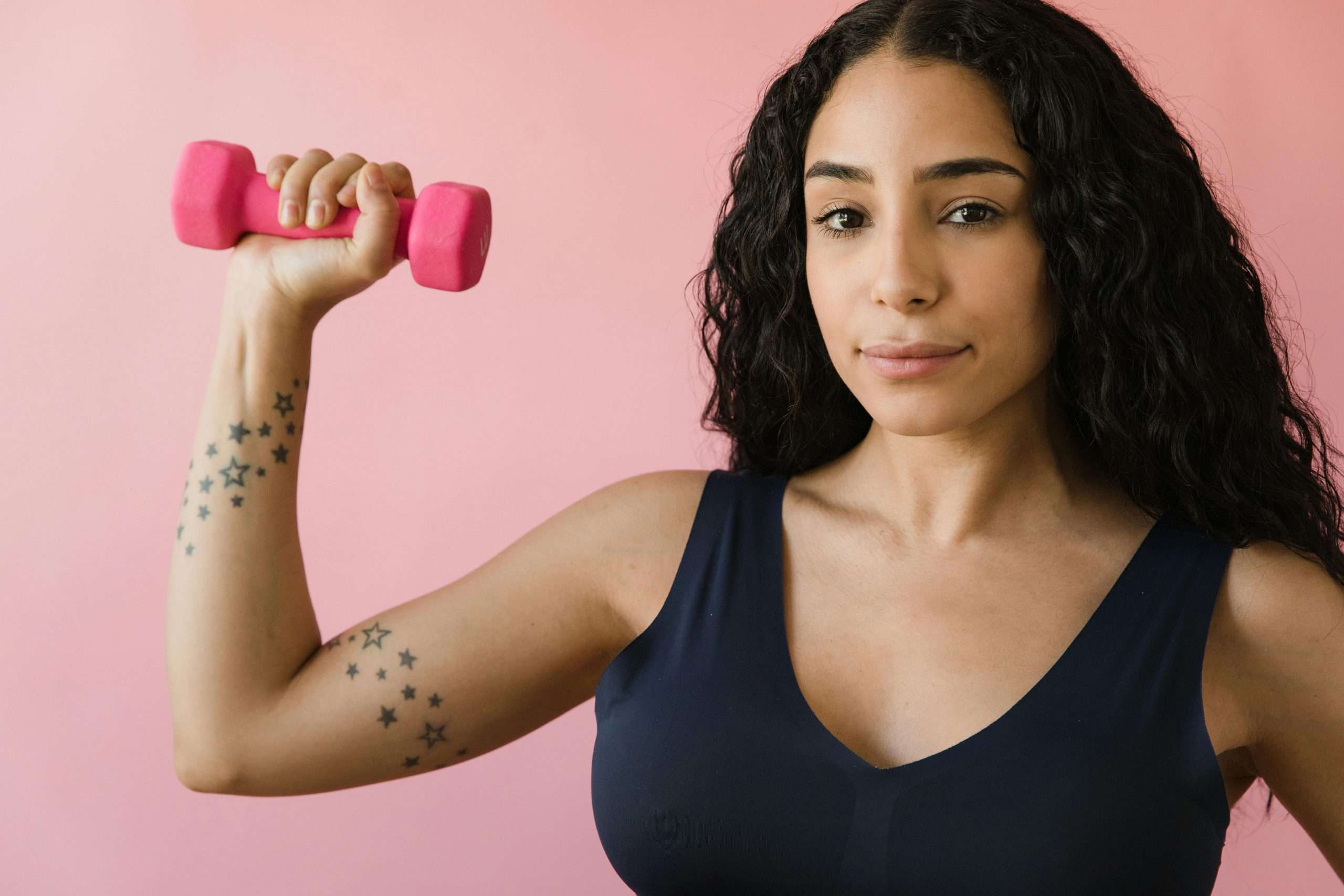woman in a blue tank top holding a pink dumbbell