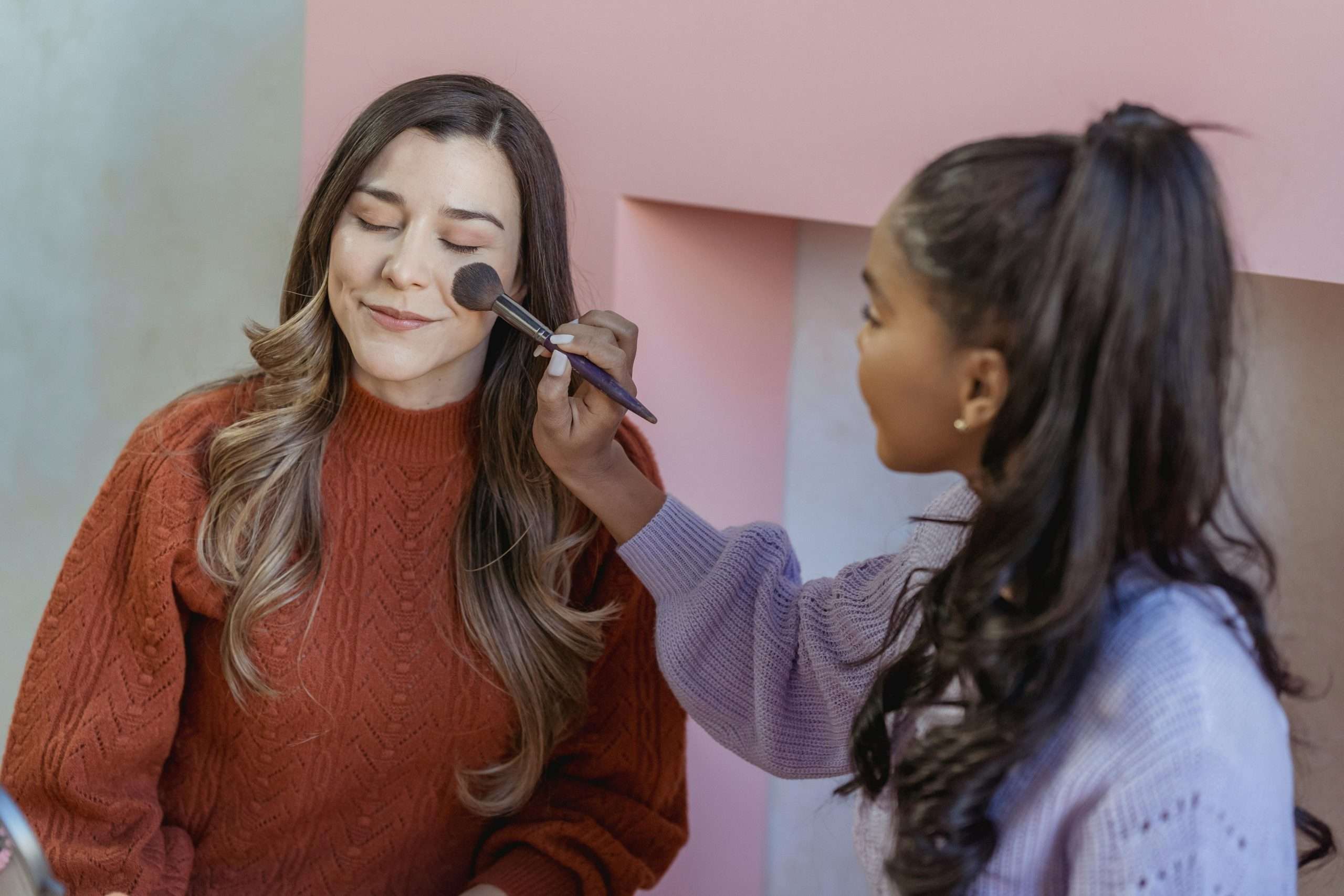ethnic lady applying foundation on the face of a friend with a brush