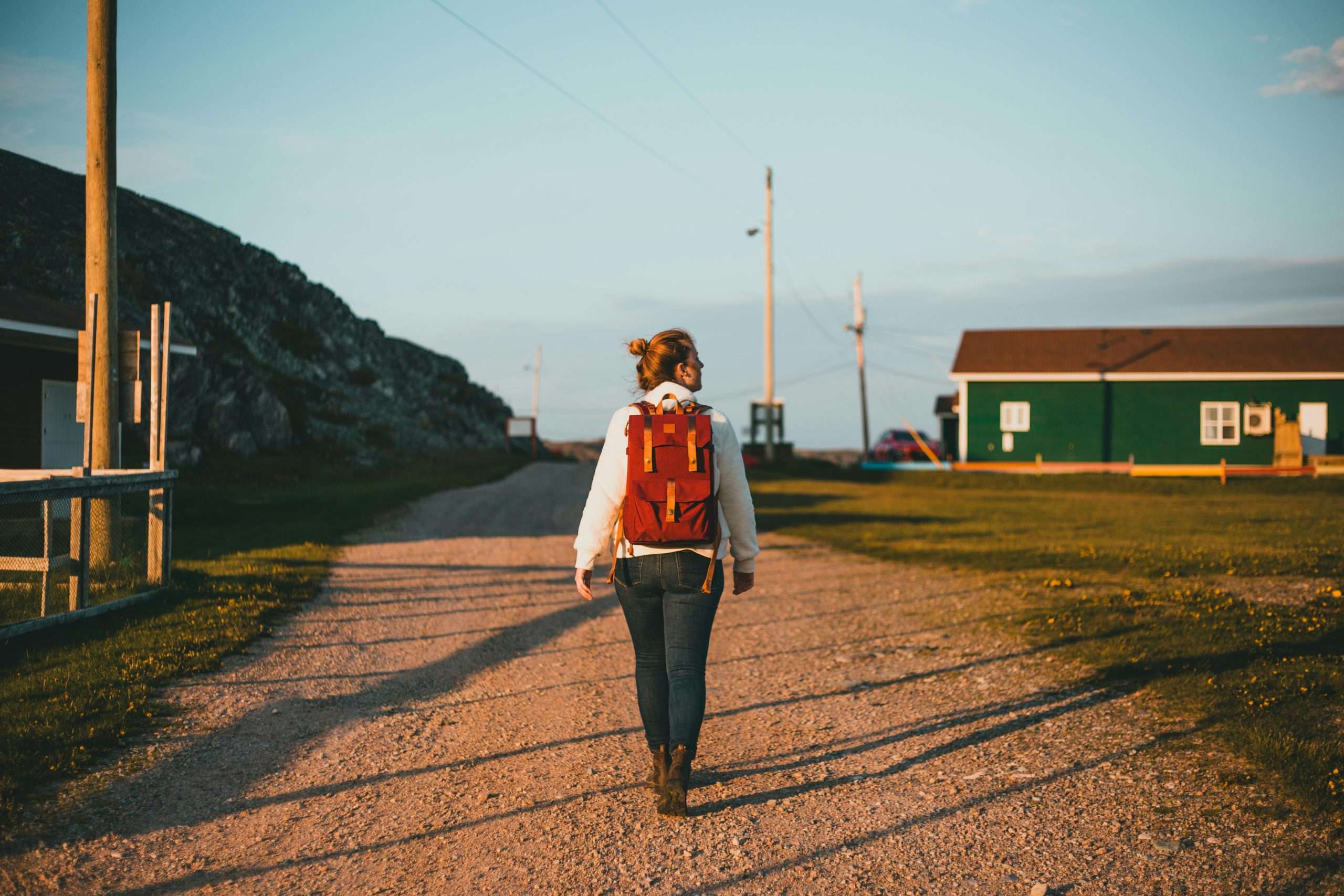 a woman with a red backpack walking on an unpaved road