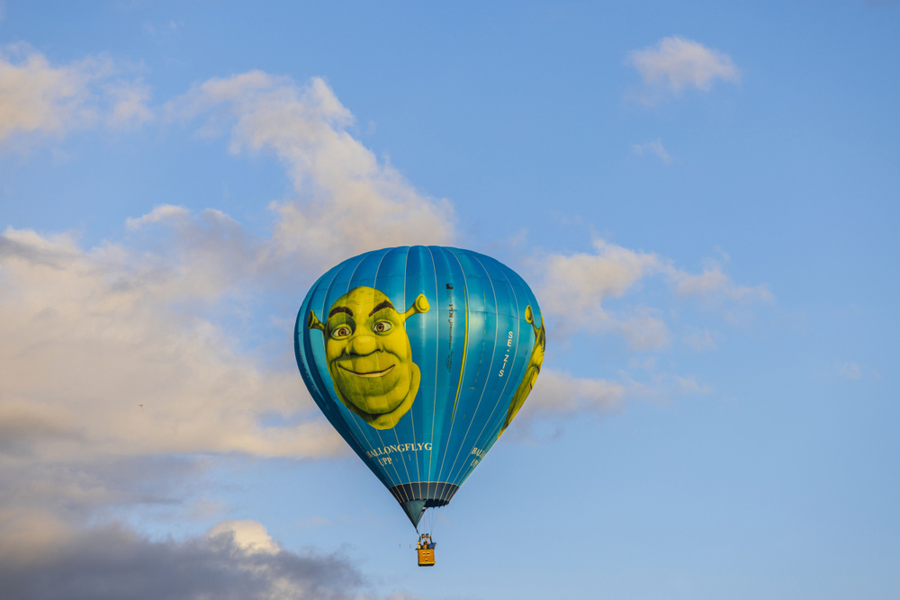 Sweden. Uppsala. 06.18.2022. Beautiful view of people flying in Shrek hot air balloon far away in blue sky with white clouds