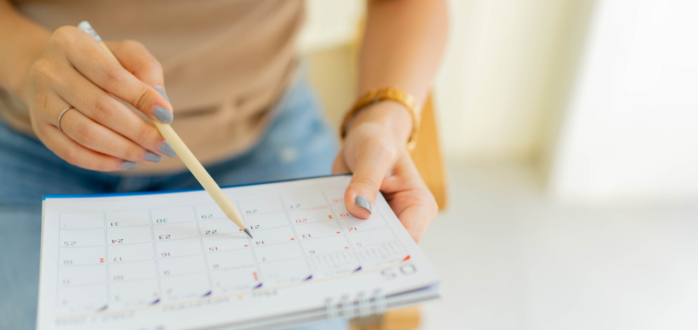 Close up on senior employee woman hand using pen to writing schedule on calendar to make appointment meeting or manage timetable each day at house for work from home concept